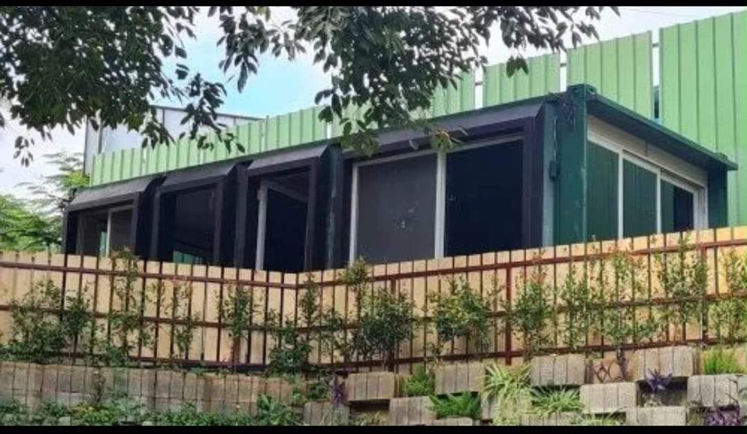 Black-and-green container bungalow above a landscaped retaining wall